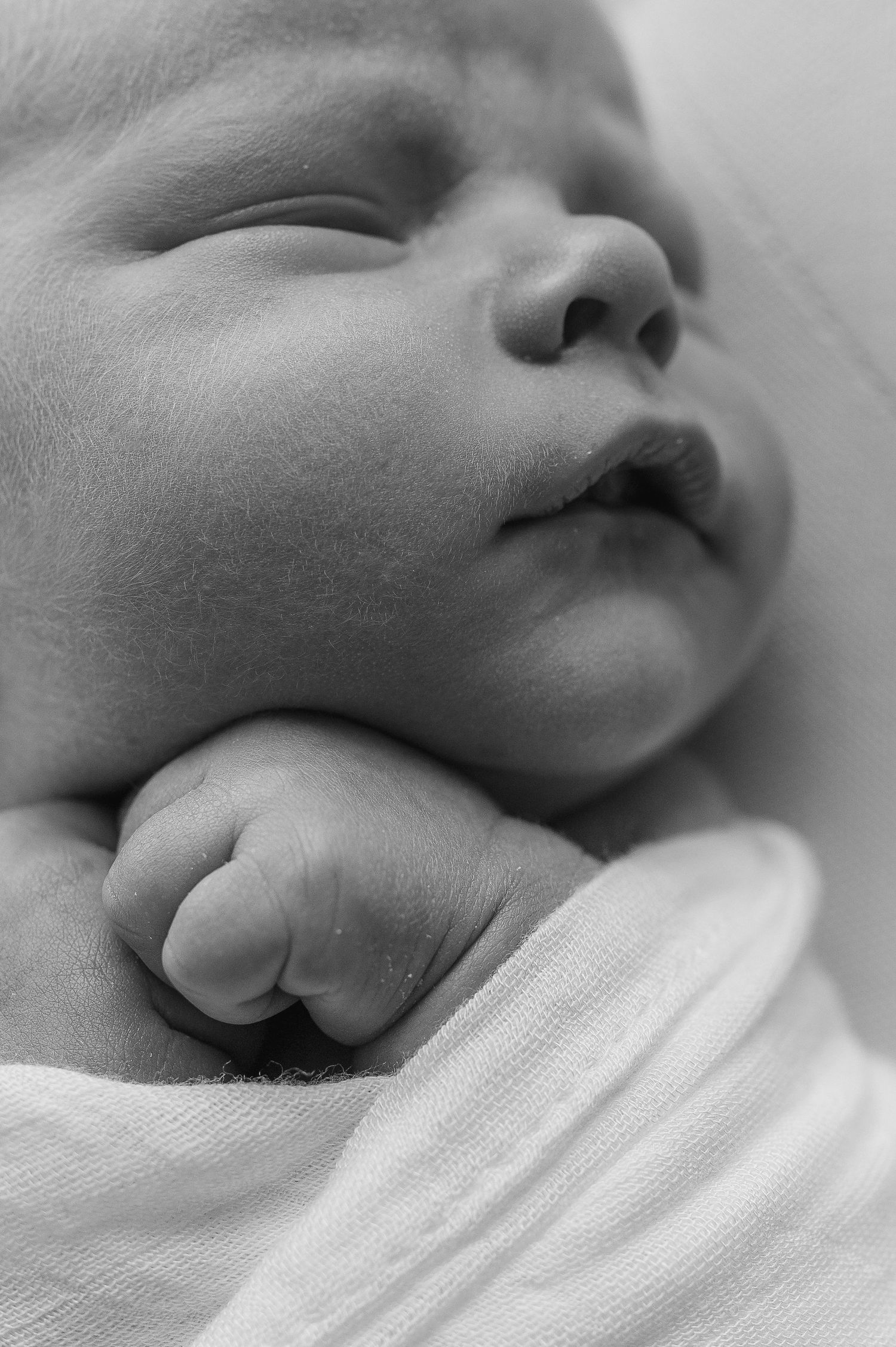 Close-up black and white portrait of sleeping newborn baby's face and tiny hand.
