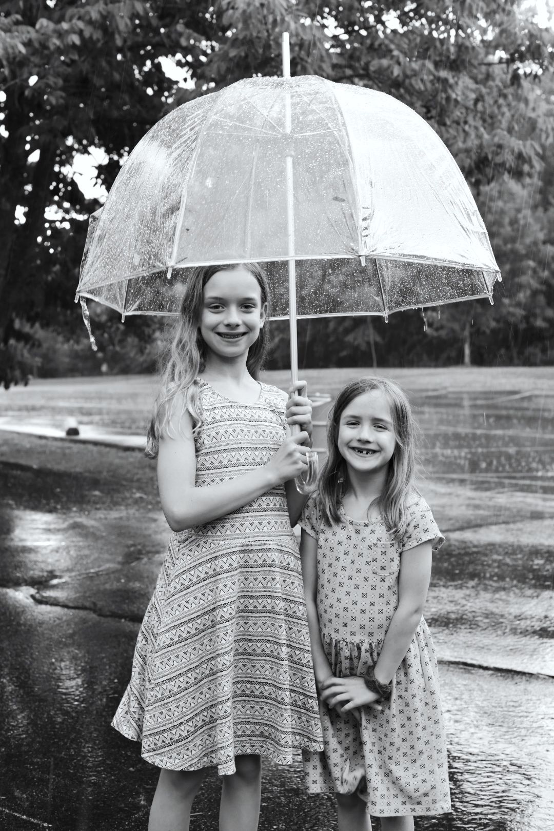 Children holding clear umbrellas playing in the rain on wet pavement.