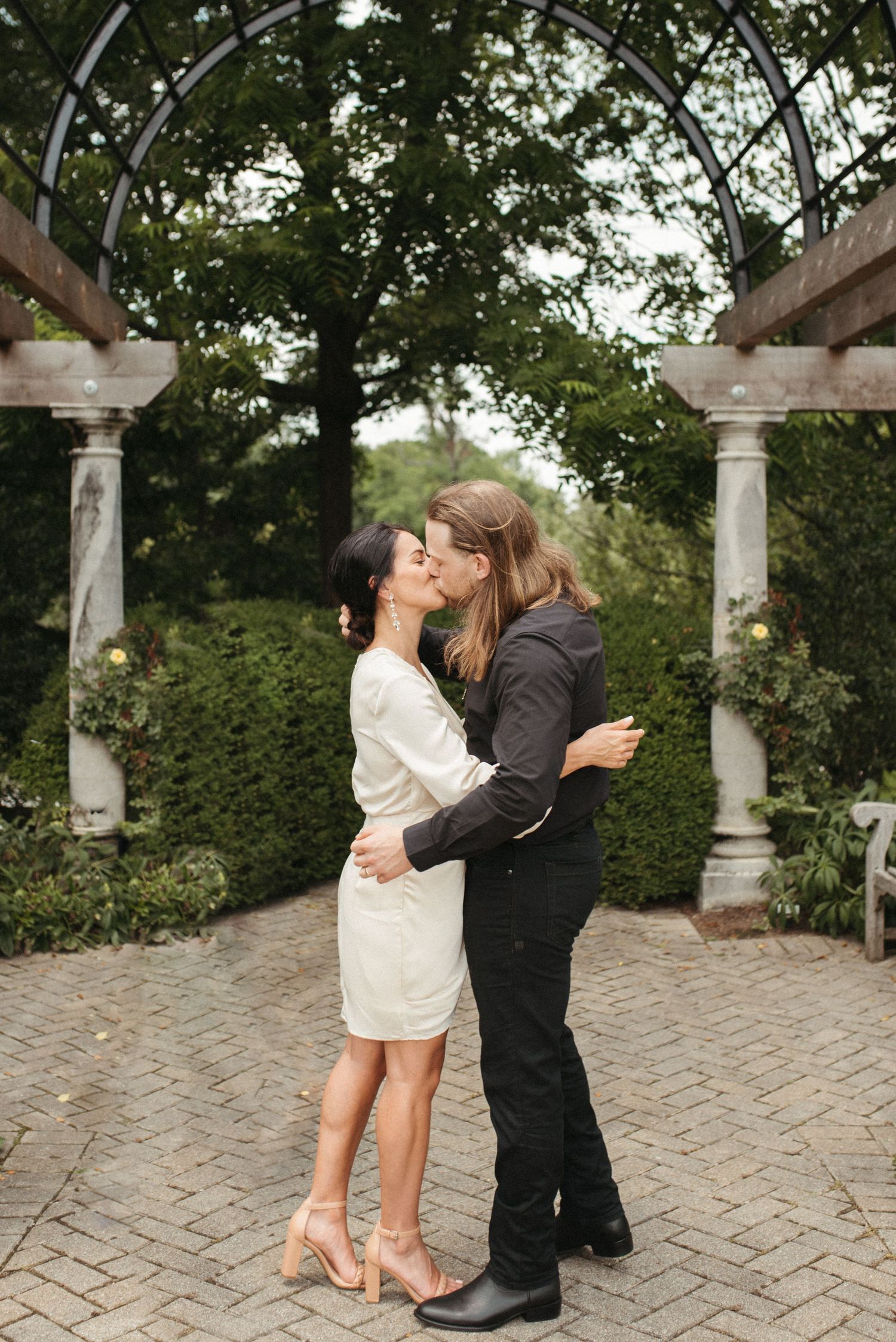 A romantic moment shared under a garden archway with stone columns.