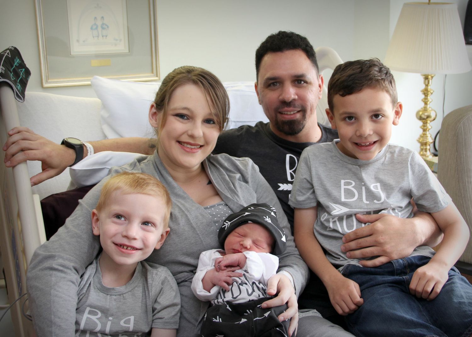 A family of five wearing matching grey outfits poses together on a couch.