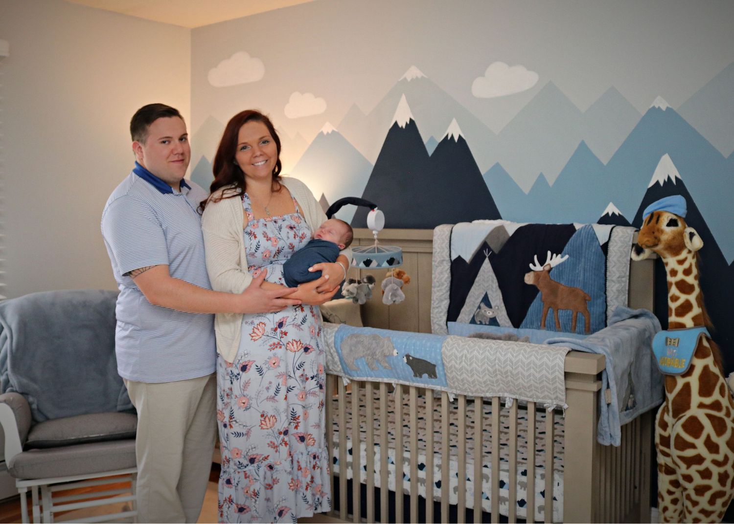 A mountain-themed nursery featuring woodland creatures and a tall giraffe decoration.