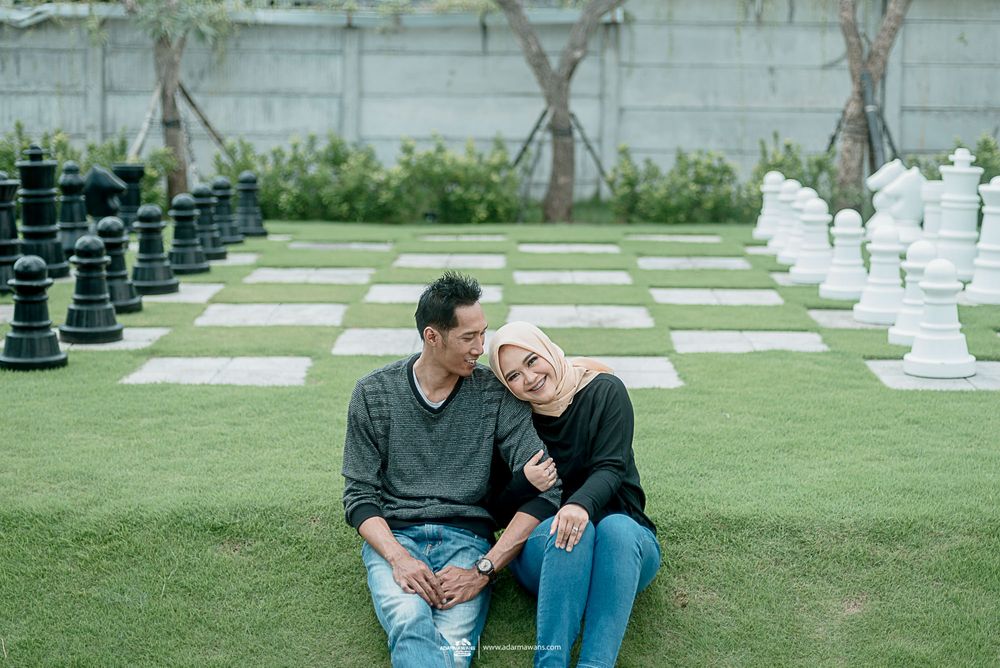 A couple relaxes on grass near giant chess pieces in an outdoor garden setting.