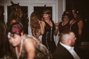 Party guests in 1920s themed attire dancing and socializing at an evening celebration.