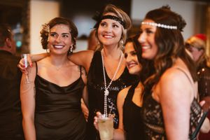 Three friends in 1920s inspired dresses smile and celebrate at a Gatsby themed party.