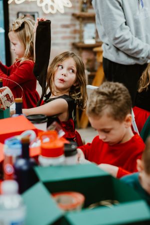 Children in red outfits participate in holiday activities at a decorated table.