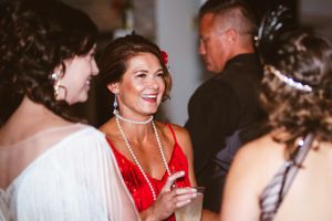 Partygoers in vintage-inspired attire laugh and socialize at a glamorous evening event.