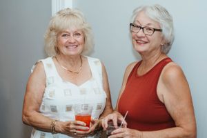 Two friends in summer attire sharing drinks and laughs together.