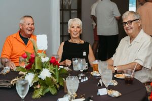 Three guests enjoying conversation and drinks at a dinner party with floral centerpiece.