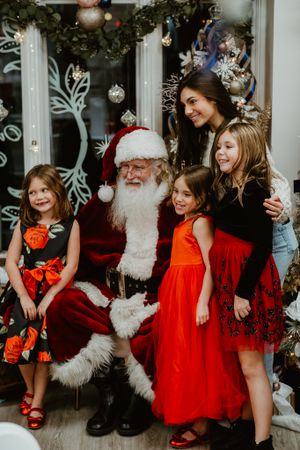 Holiday photo with Santa Claus and festively dressed people in front of decorated window with ornaments.