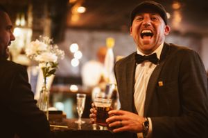 Person laughing joyfully at a formal event while holding a drink at an elegant bar.