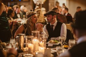 Couple in vintage attire shares an intimate moment at a candlelit dinner party.