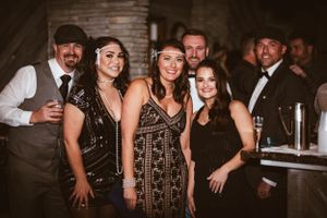 A group poses together at a vintage-themed party wearing art deco style formal attire.