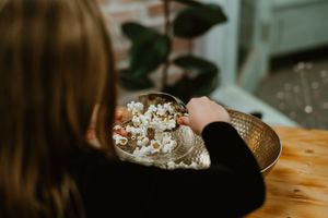 Person reaching for popcorn in a wooden bowl on wooden table.