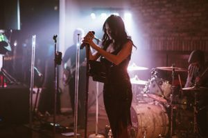 A performer stands in atmospheric stage lighting while audience members watch.