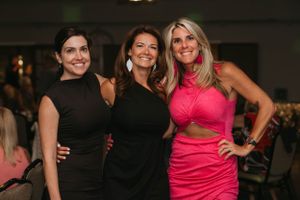 Three women in elegant evening wear pose together at a social gathering.