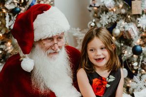 Santa Claus in traditional outfit shares joyful moment near Christmas tree.