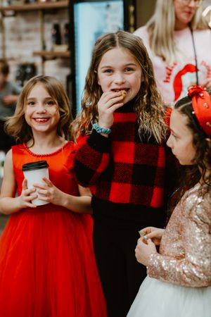 Girls in festive holiday outfits sharing excited expressions at winter celebration.