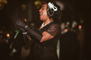 A performer in vintage attire with white feather headpiece sings passionately at an event.