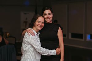 Two people embrace in a friendly pose at an indoor social gathering.