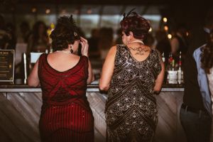 Two guests in vintage-style dresses sit at the bar during an evening party.