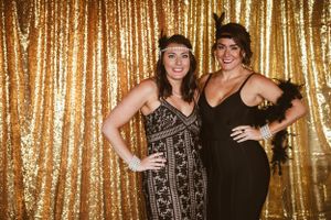 Two friends posing in formal dresses against a gold sequin backdrop.