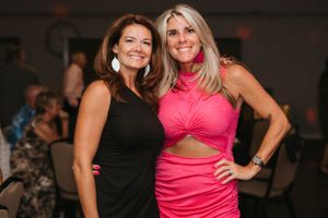 Two women in contrasting black and pink dresses pose together at a party.
