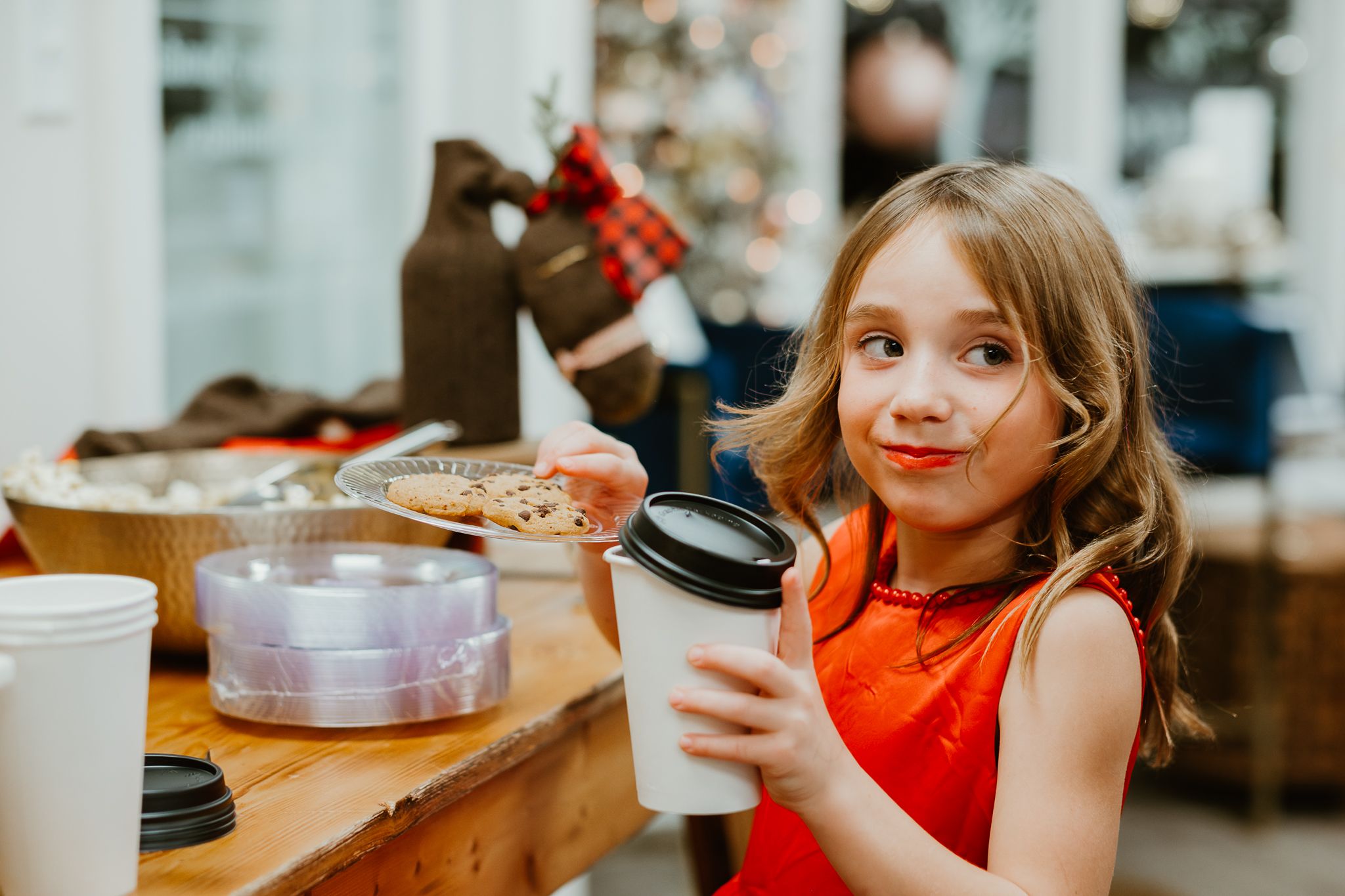 Child in red dress holds drink cup during holiday celebration.