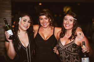 Three friends in beaded flapper dresses celebrate at a 1920s themed party.