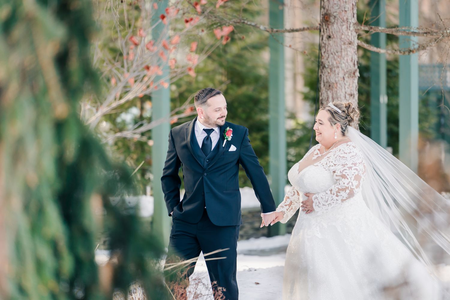 A winter wedding couple walking through evergreen trees in fresh snow.