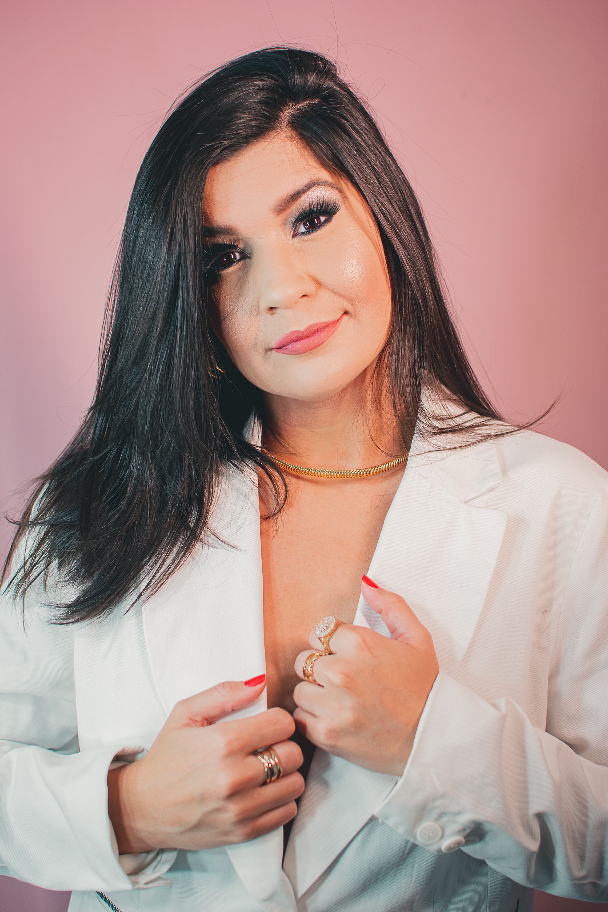 Elegant portrait showing woman in white blazer with flowing dark hair against pink backdrop.