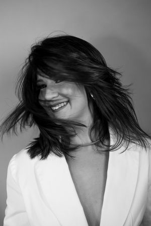 Black and white portrait capturing joyful movement with windswept hair and white blazer.