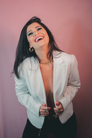 Candid fashion portrait with genuine laughter against pink background wearing white blazer.