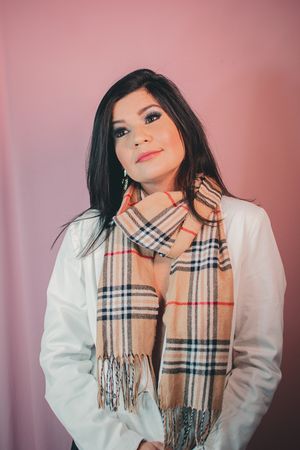 Fashion portrait featuring classic plaid scarf and white blazer against pink background.