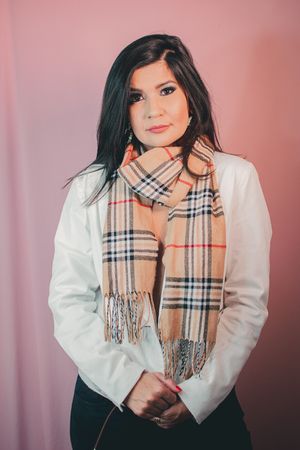 Sophisticated pose in white blazer and designer plaid scarf against soft pink backdrop.