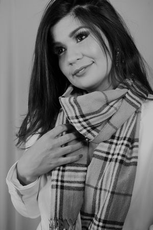 Black and white portrait wearing plaid scarf and white blazer with subtle smile.