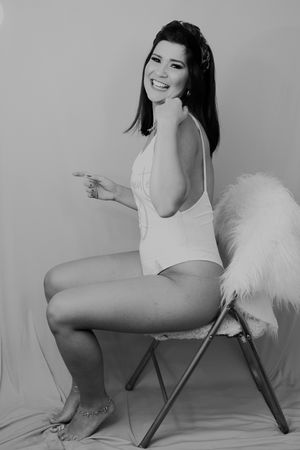 Vintage-inspired boudoir photo in white bodysuit on chair with feather prop.