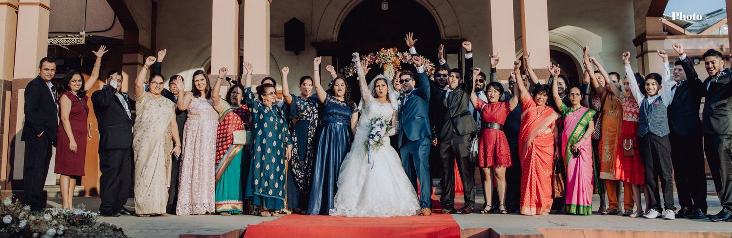 Large group wedding photo with guests gathered outside a church building.