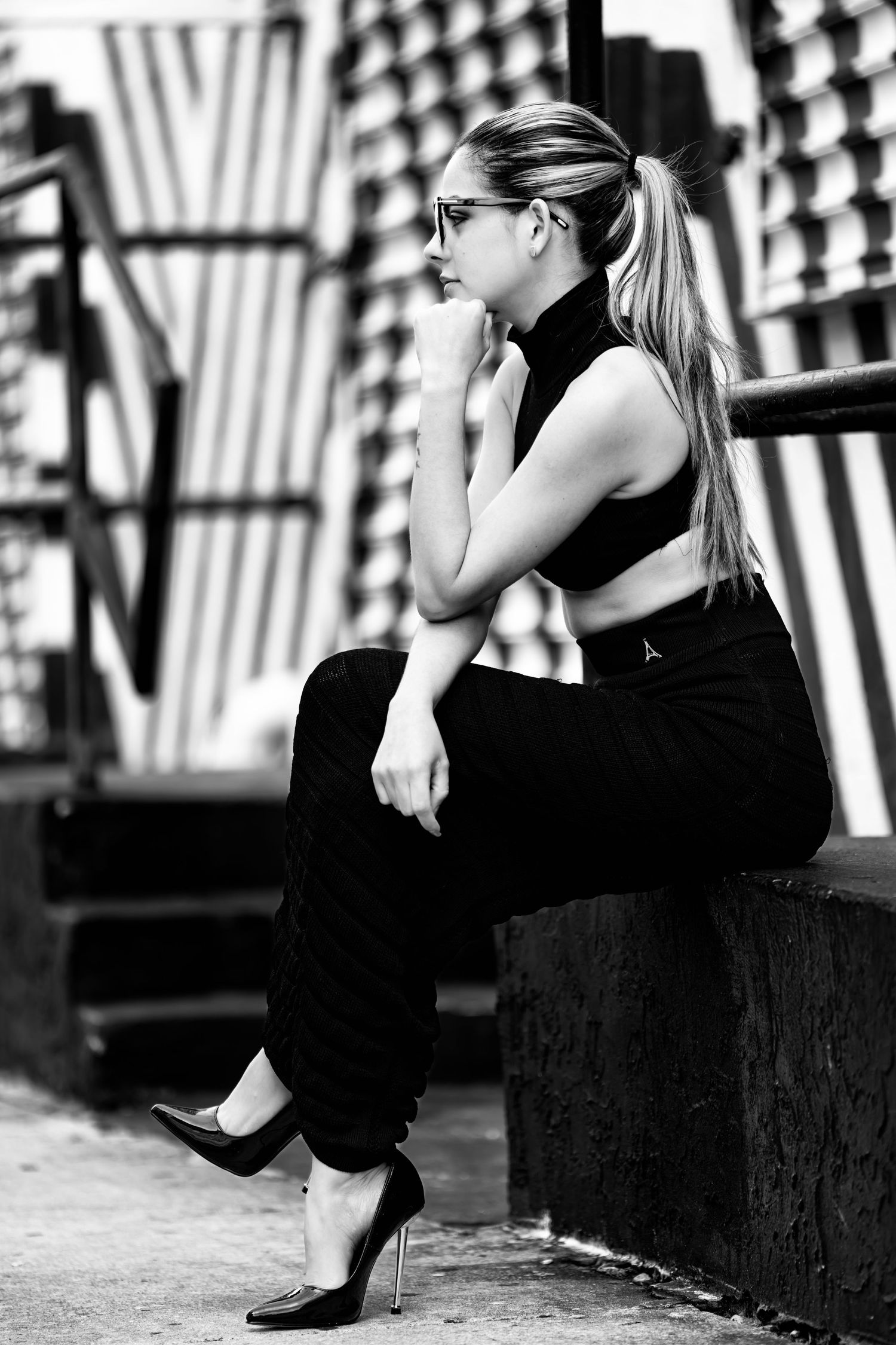 Black and white photo of person in black dress sitting on bench with dramatic shadows.