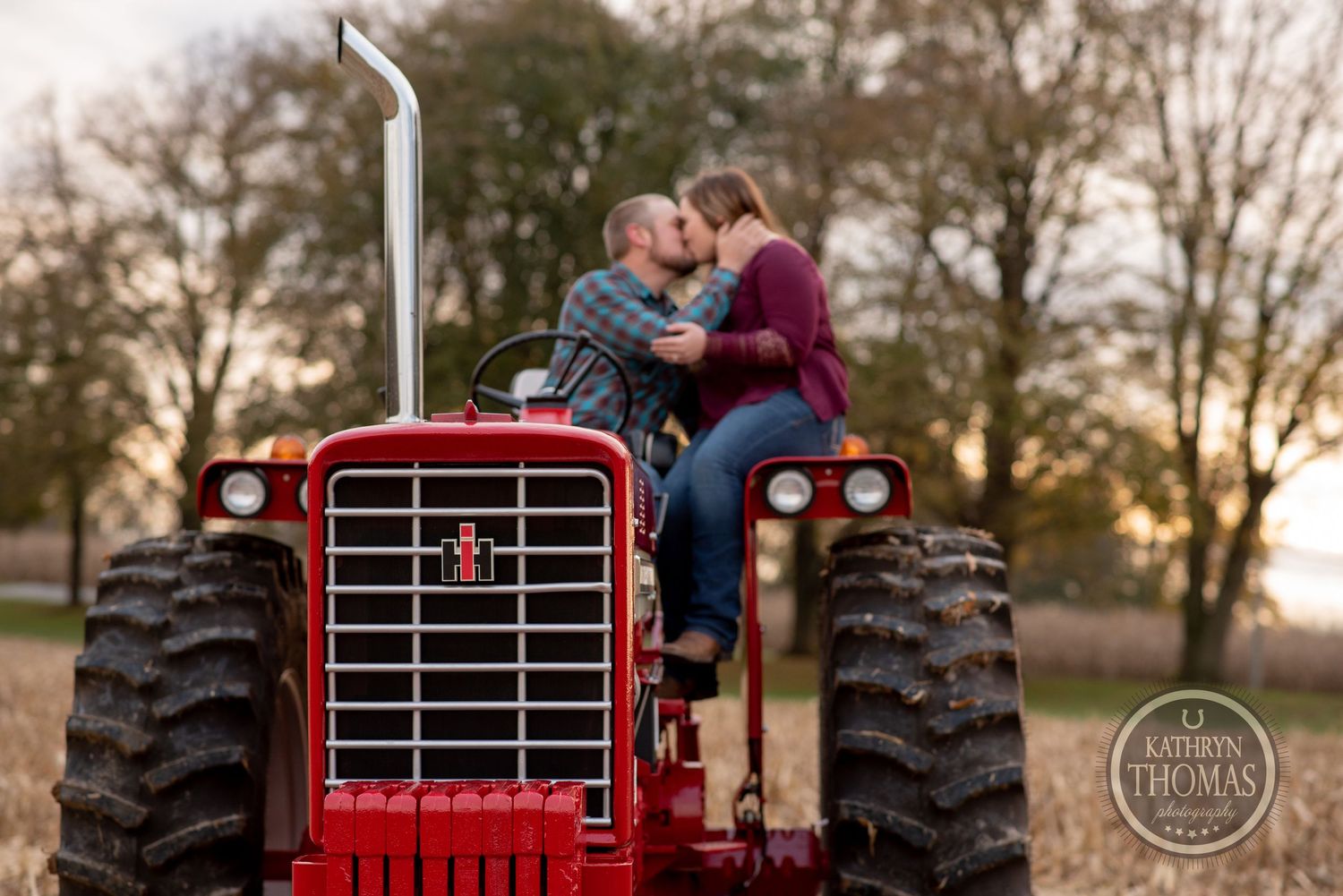A couple embraces while sitting on a red vintage tractor during golden hour.