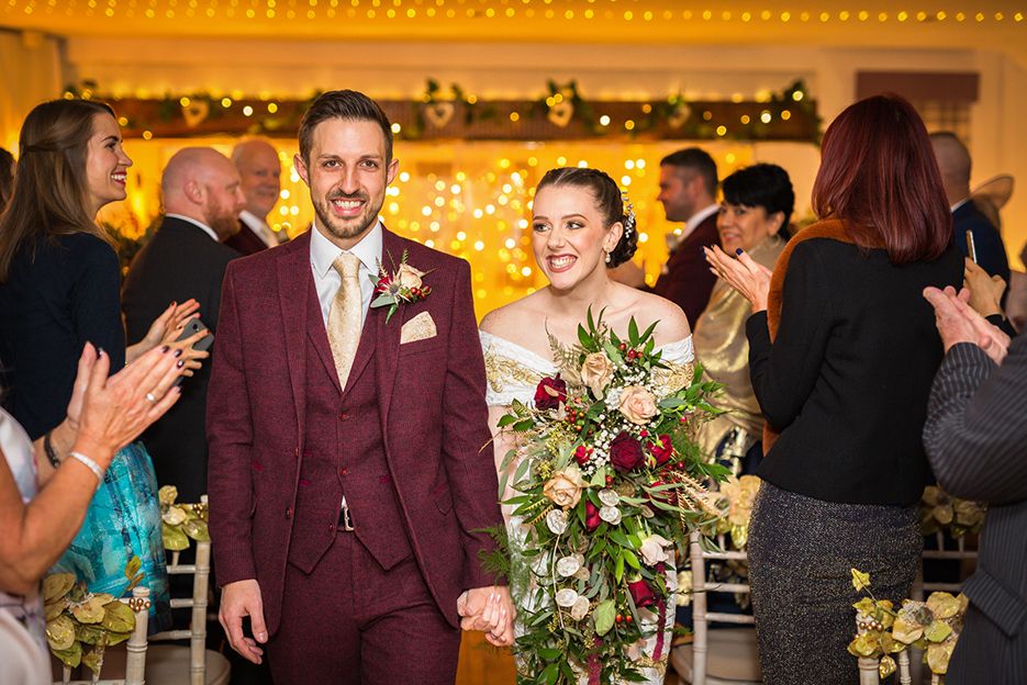 A smiling bride and groom walk up the aisle at the Lyme Breeze wedding venue in Cheshire