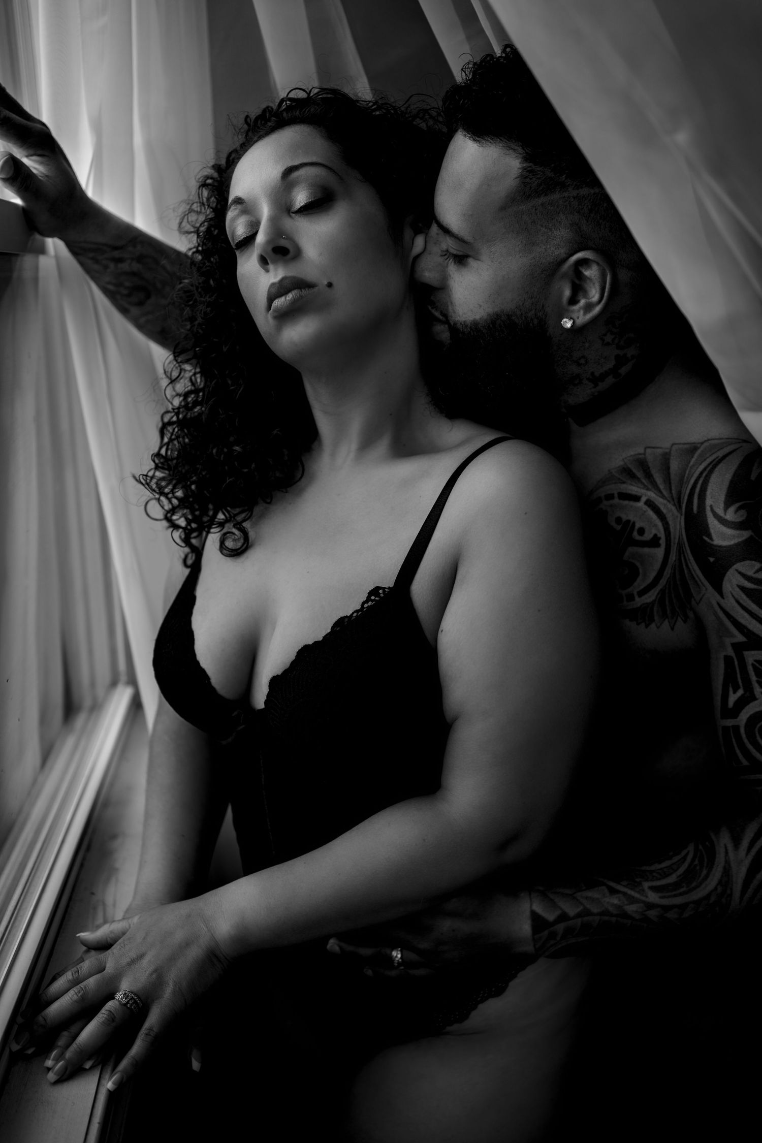 Intimate black and white boudoir photography with dramatic window lighting.