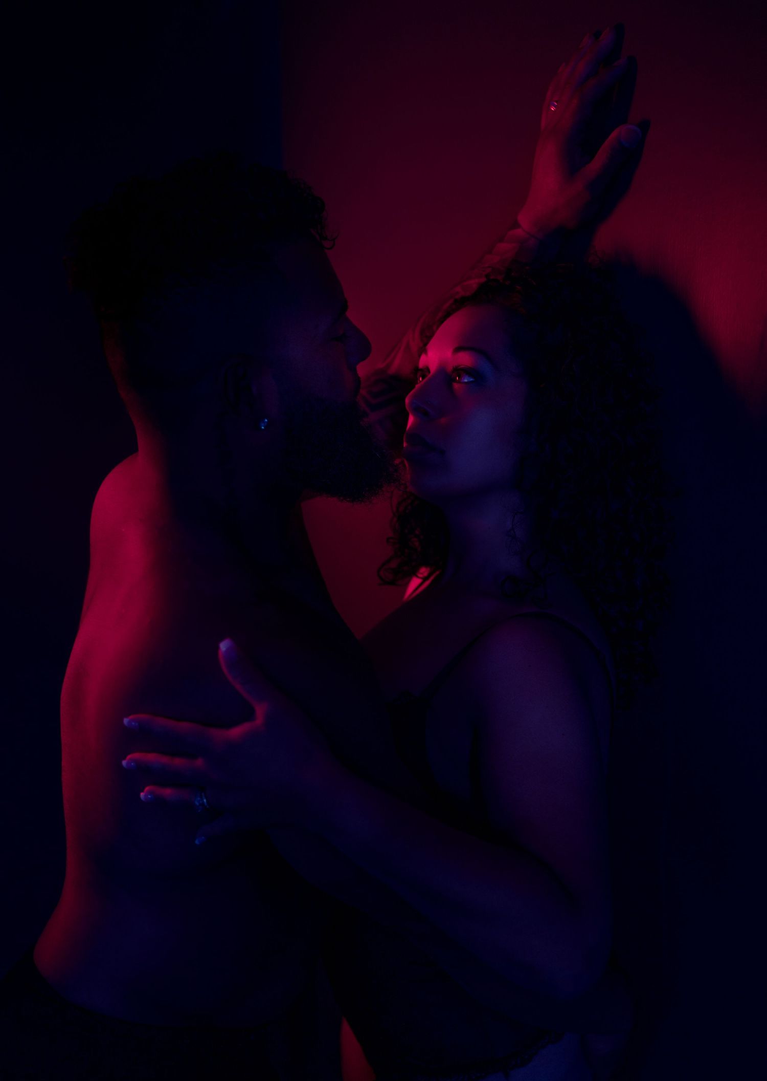 Artistic silhouettes against deep red and blue lighting in dark setting.