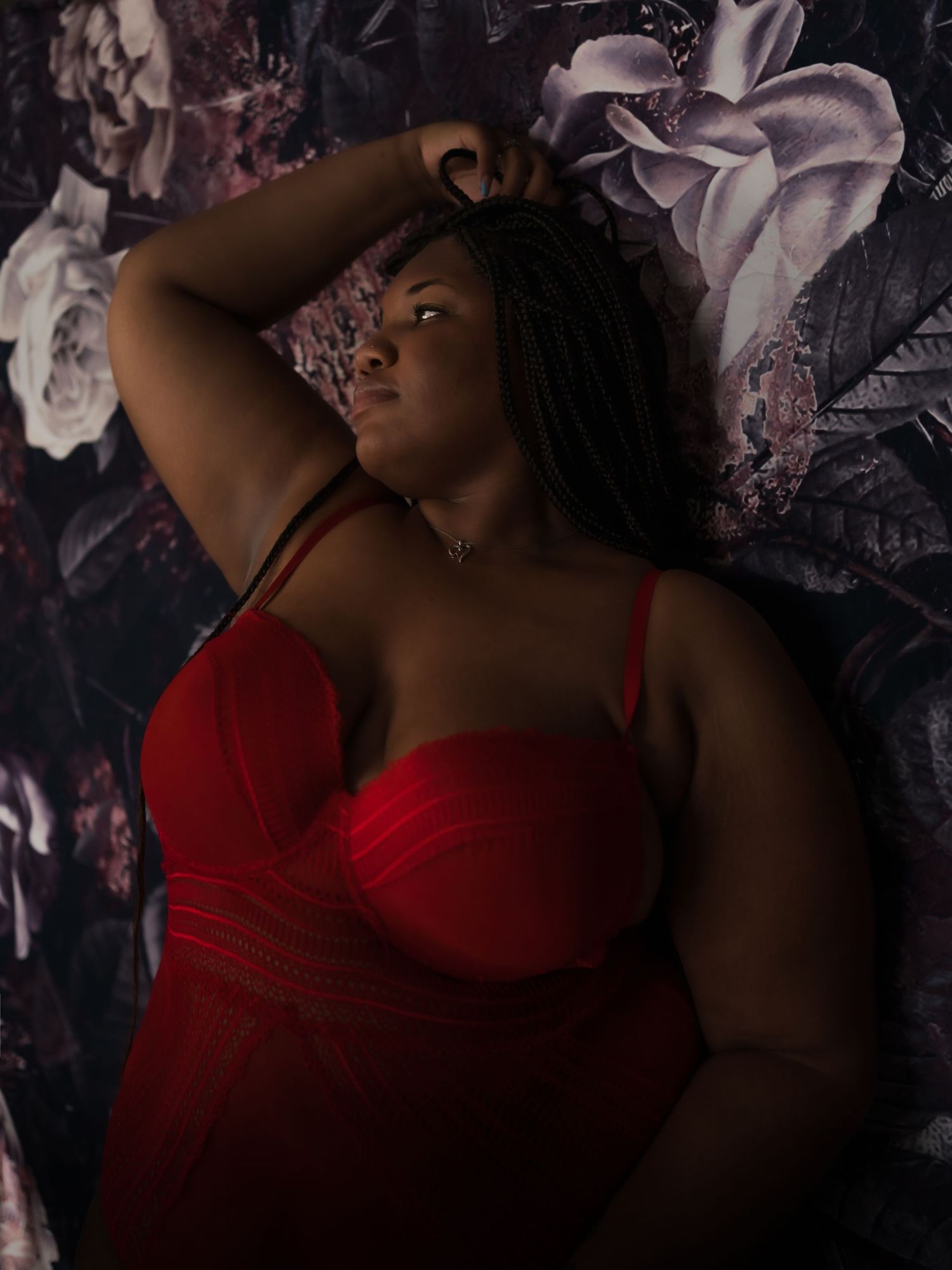 Dramatic boudoir portrait with red lingerie against floral backdrop.