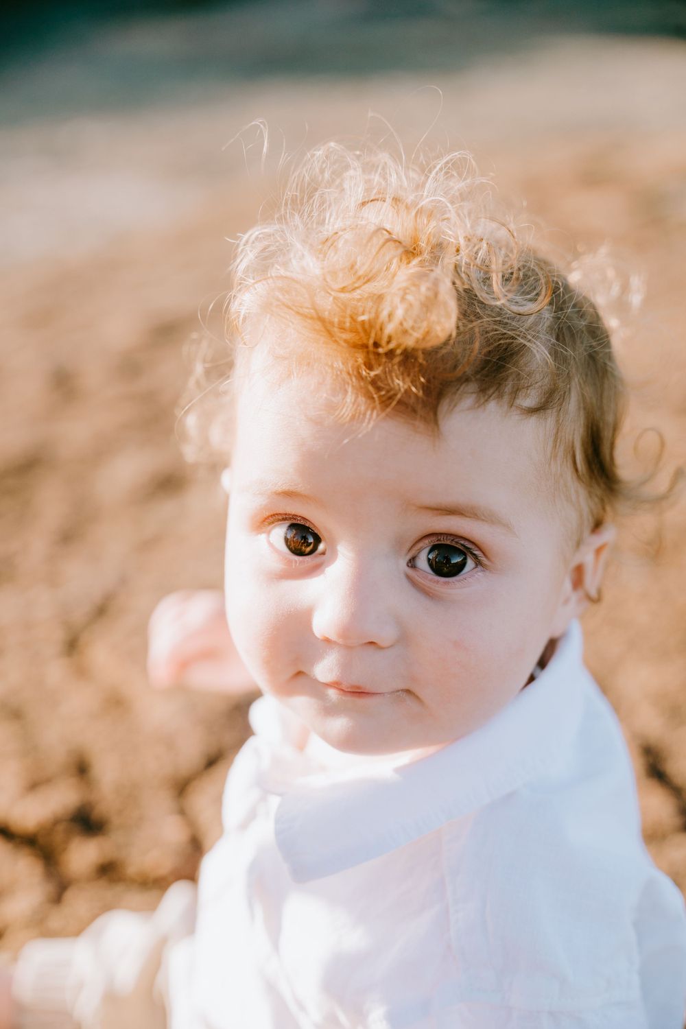 A close-up portrait of a young child in white clothing with curly hair and bright eyes.
