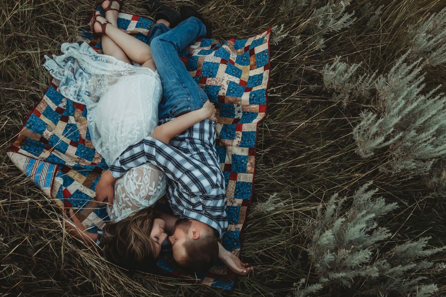 A couple laying on a colorful quilt blanket in nature during a romantic photoshoot.