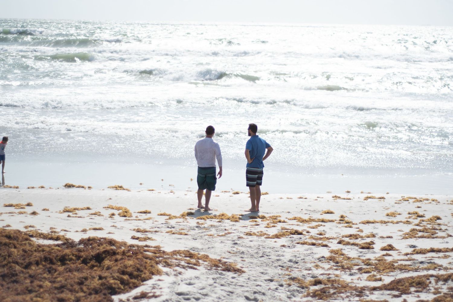 Two people standing on beach watching waves crash against shore.