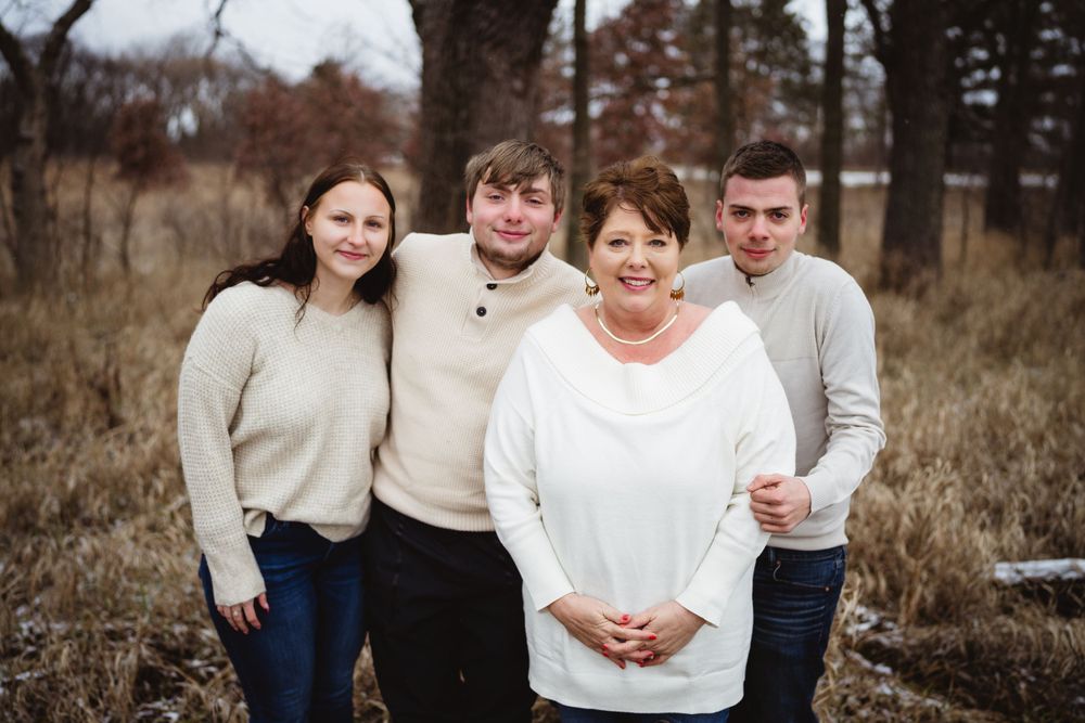 Small group posed together outdoors in neutral-colored sweaters against bare winter trees.
