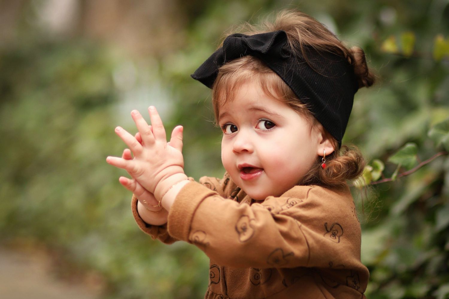 A candid moment captures excitement with hands clapping in a brown sweater outdoors.