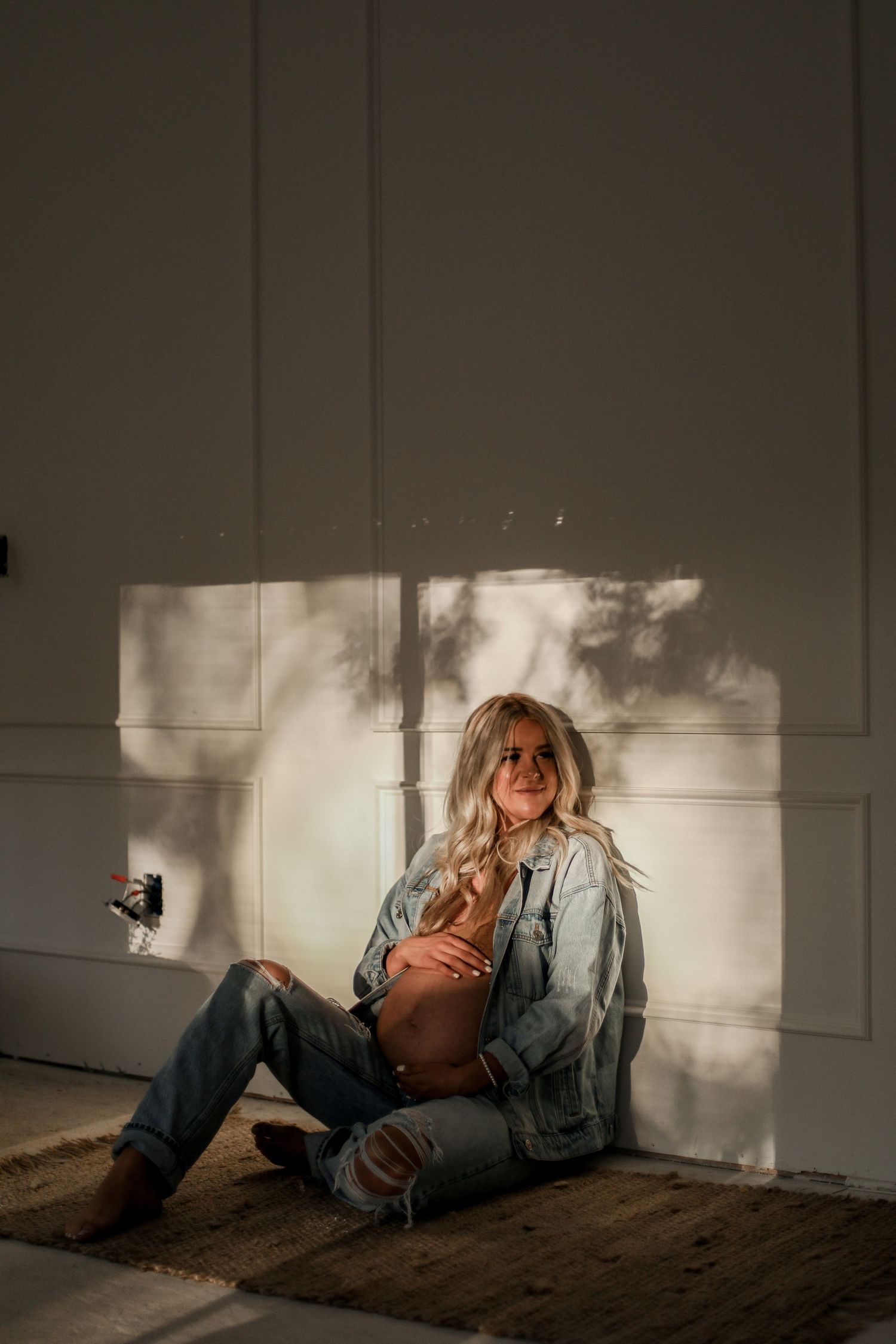 Artistic maternity portrait with dramatic window light shadows on white wall.