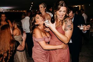 Wedding guests dancing and celebrating in dusty rose dresses at evening reception.